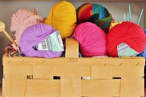 Woven basket filled with colorful yarn and knitting needles.